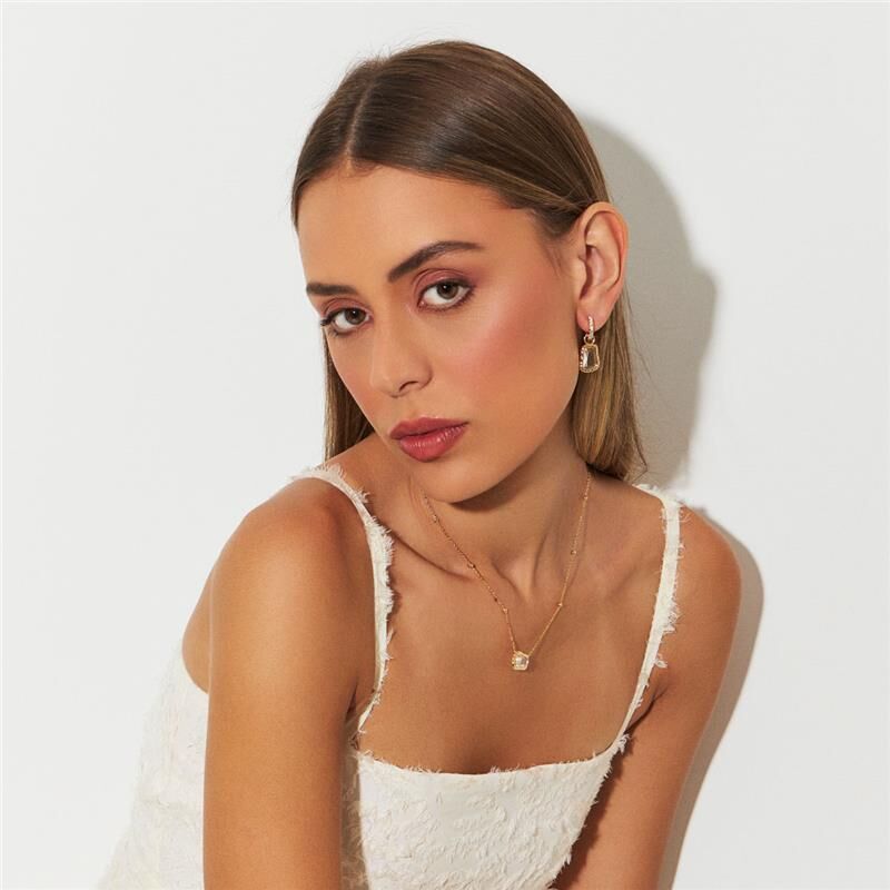 Modelo usando brinco Lumen, semijoia antialérgica, banho dourado 18k, pedra de cristal, destaque em moda sofisticada.