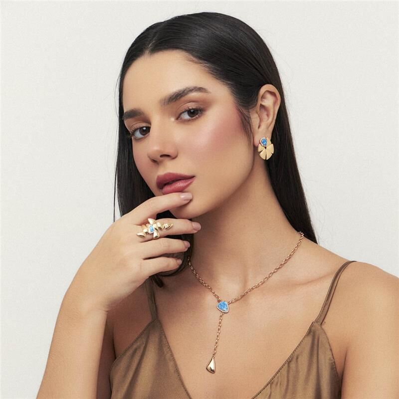 Mulher usando conjunto de semijoias douradas 18k, anel Zuri Triad, colar e brincos com cristal e zircônia. Tecnologia antialérgica.