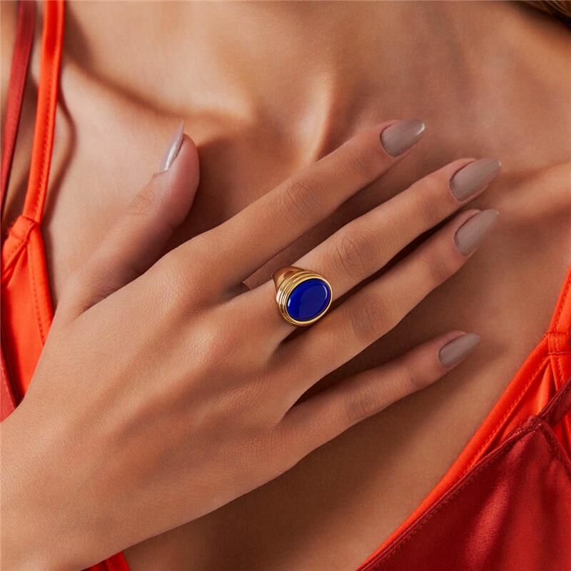 Mulher usando Anel Big Sur com cristal azul, semijoia dourada 24k antialérgica, destacando elegância e qualidade.