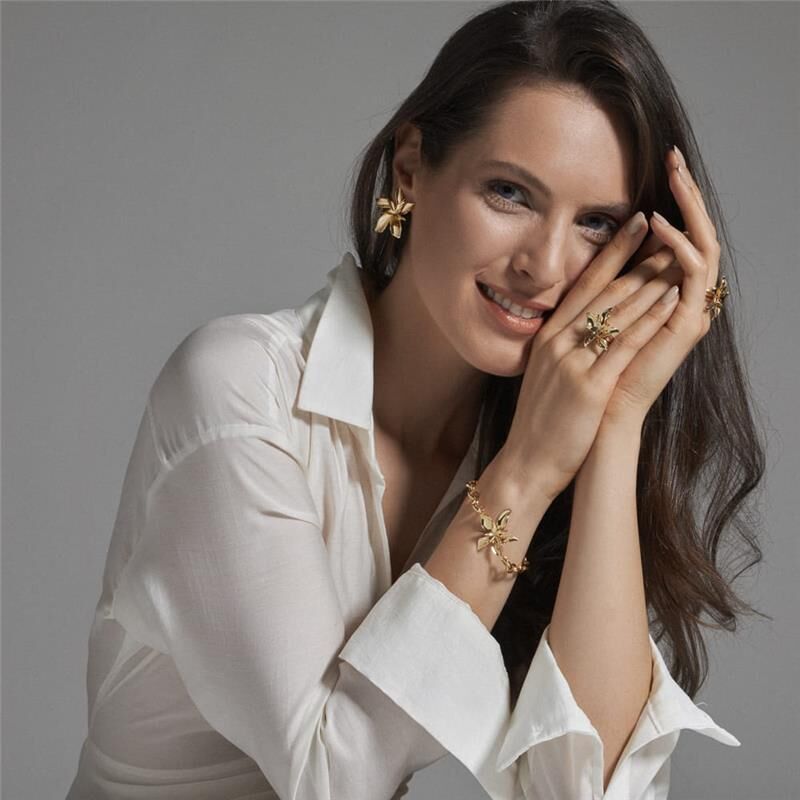 Mulher sorridente usando semijoias de alta qualidade, incluindo pulseira Orquídea Dourada, com banho de ouro 18k e 24k, antialérgica.