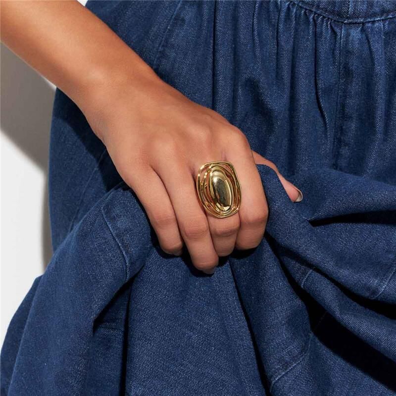 Anel Golden Eye em mão feminina, semijoia antialérgica banhada a ouro 18k, largura 2,5cm, altura 3,3cm, ideal para qualquer ocasião.