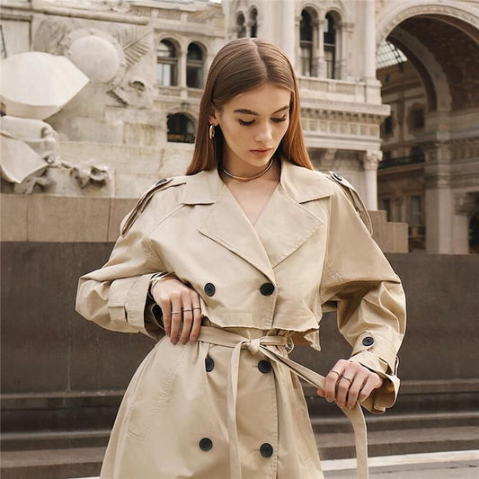 Mulher em trench coat bege usando semijoia "Choker Vibrance" antialérgica dourada e ródio, estilo elegante ao ar livre.