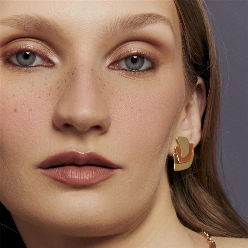 Mulher usando Brinco Terracota Curvo, semijoia de alta qualidade com banho dourado, antialérgico, 18k e 24k, elegante e moderno.