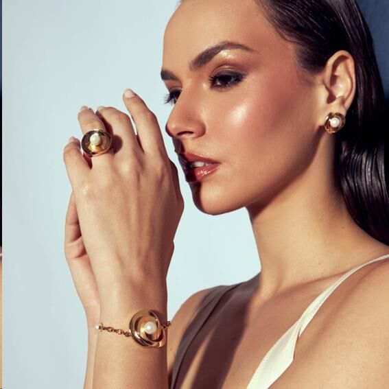Mulher elegante usando semijoias de alta qualidade com pérolas e banho em ouro dourado, incluindo pulseira e anel antialérgicos.